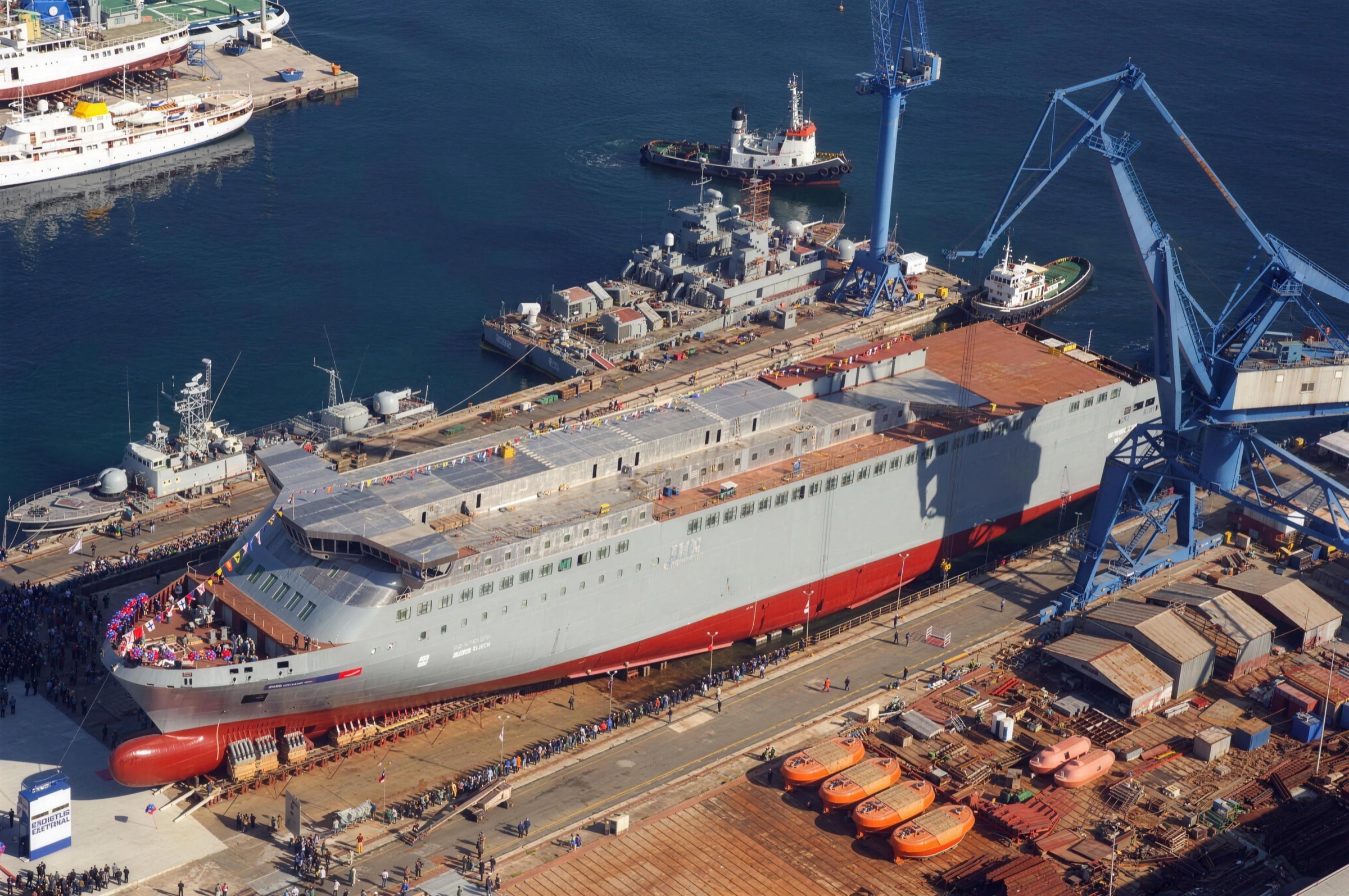 Aerial view of a ferry hull on the slipway at launch, surrounded by cranes