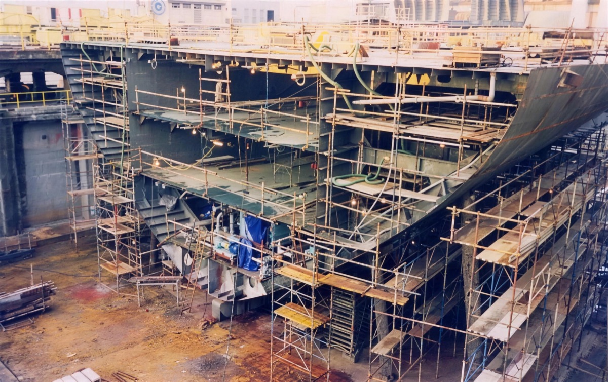 A hull under construction in dry dock, wrapped in scaffolding